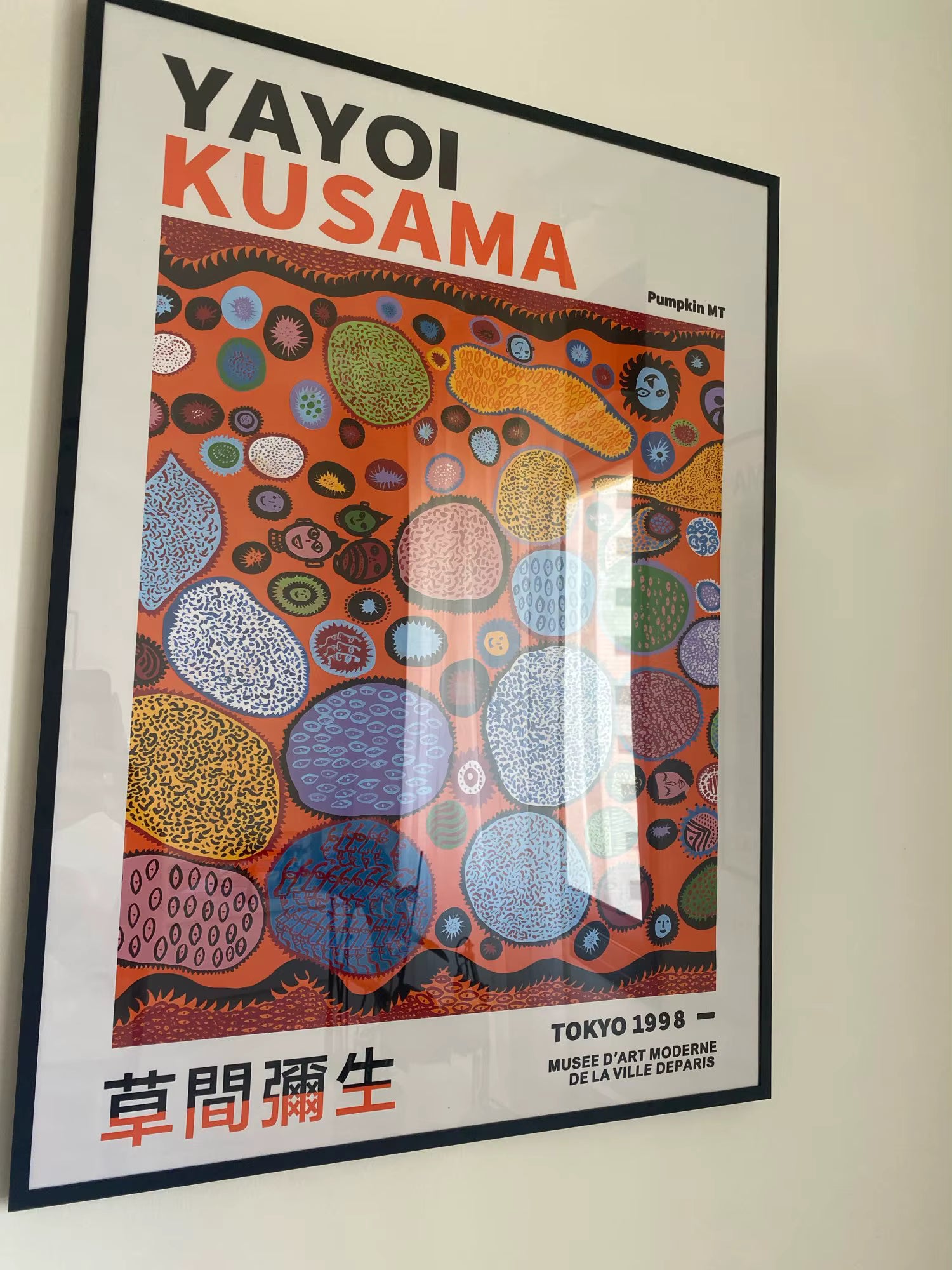 Framed Yayoi Kusama artwork with colorful abstract design on a beige wall.
