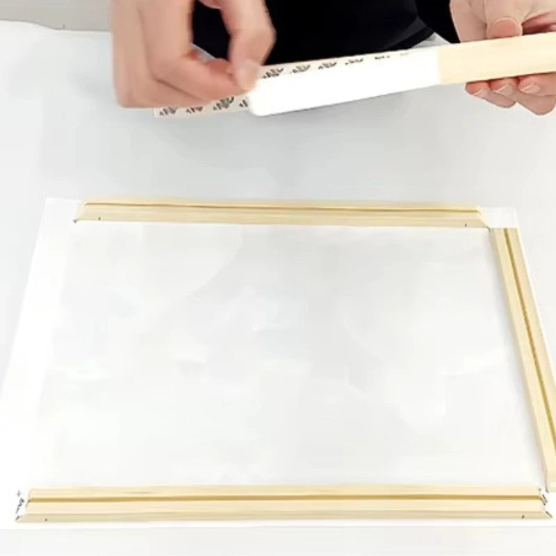 Person assembling a wooden frame with white paper on a white background