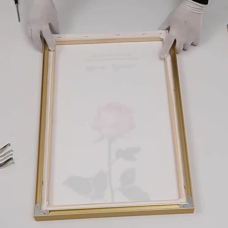 Wooden picture frame with glass on a white surface, held by hands wearing gloves.