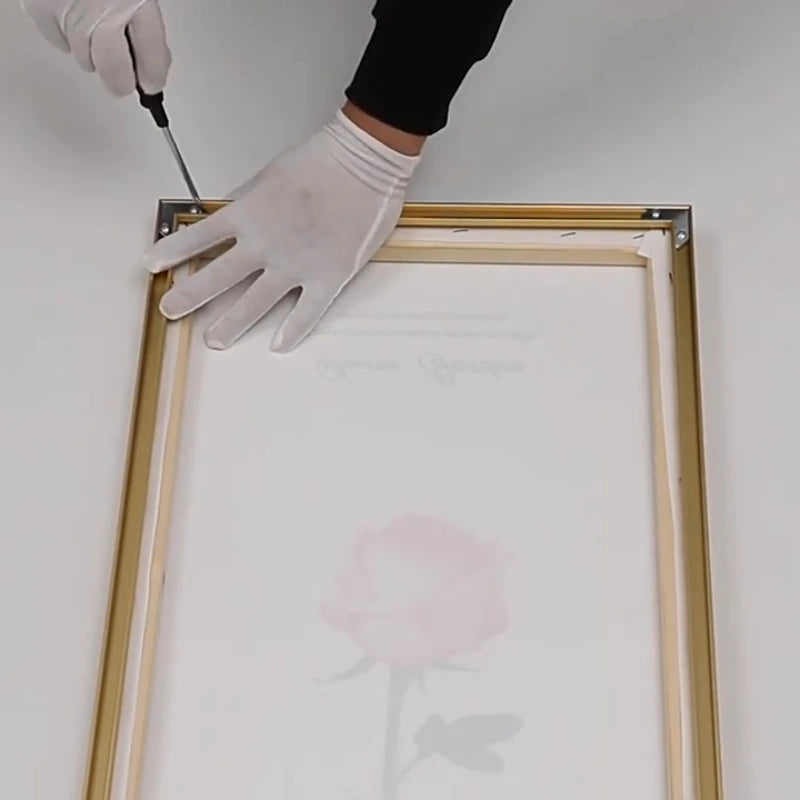 Person wearing gloves and using a screwdriver to assemble a wooden picture frame.