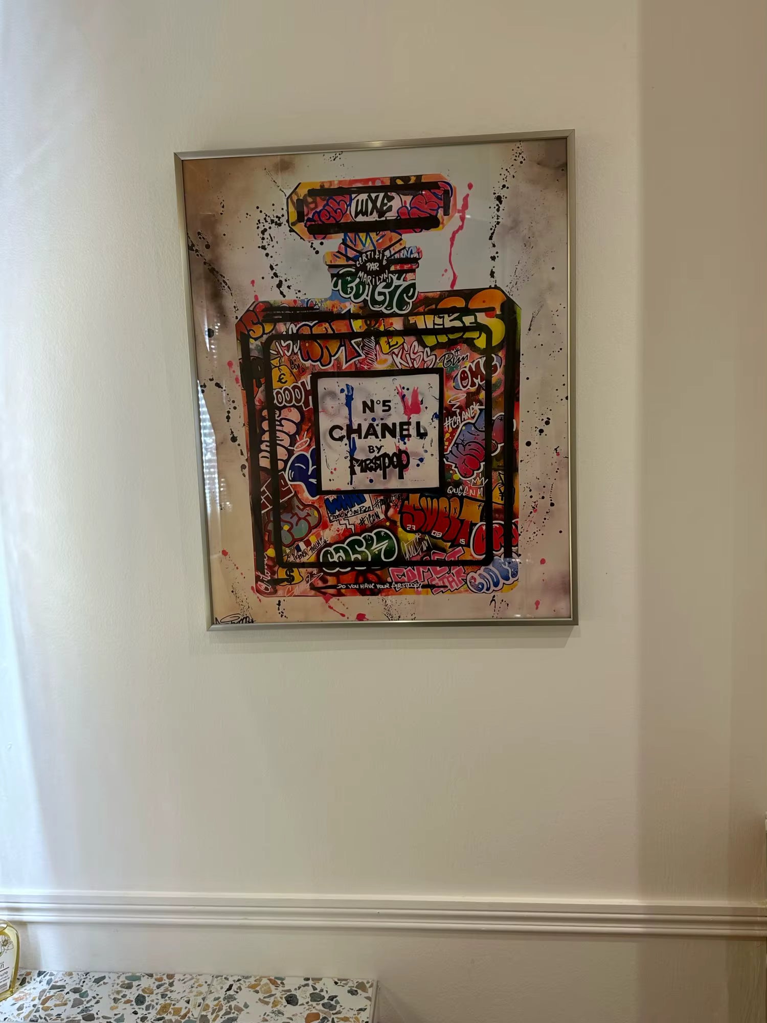 Framed artwork of a colorful Chanel perfume bottle on a wall.