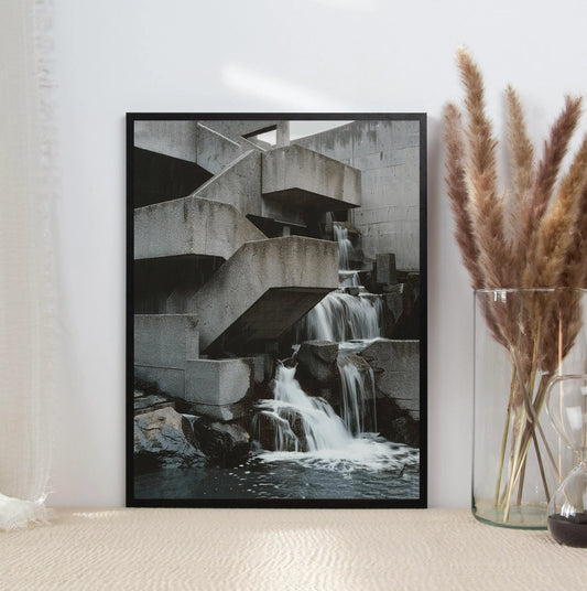 Framed black and white photograph of a waterfall on a wall next to a vase with dried plants. Canvas & Curio