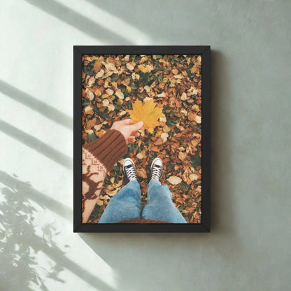 Framed photo of a person holding a yellow leaf on a ground covered with autumn leaves.