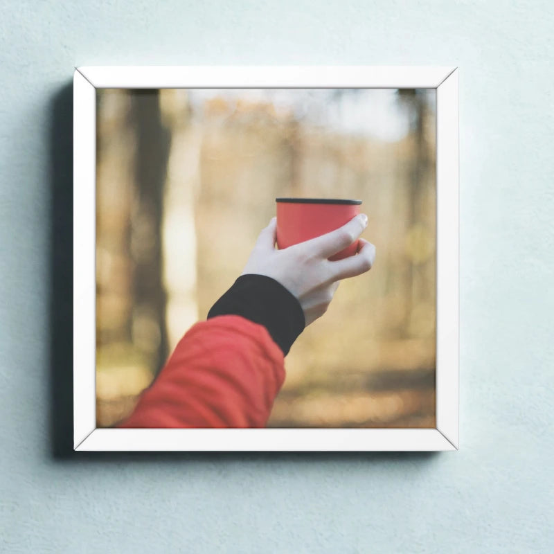 Framed picture of a hand holding a red cup in a forest setting