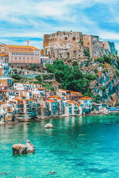 Village by the sea with a castle on a hill under a blue sky.