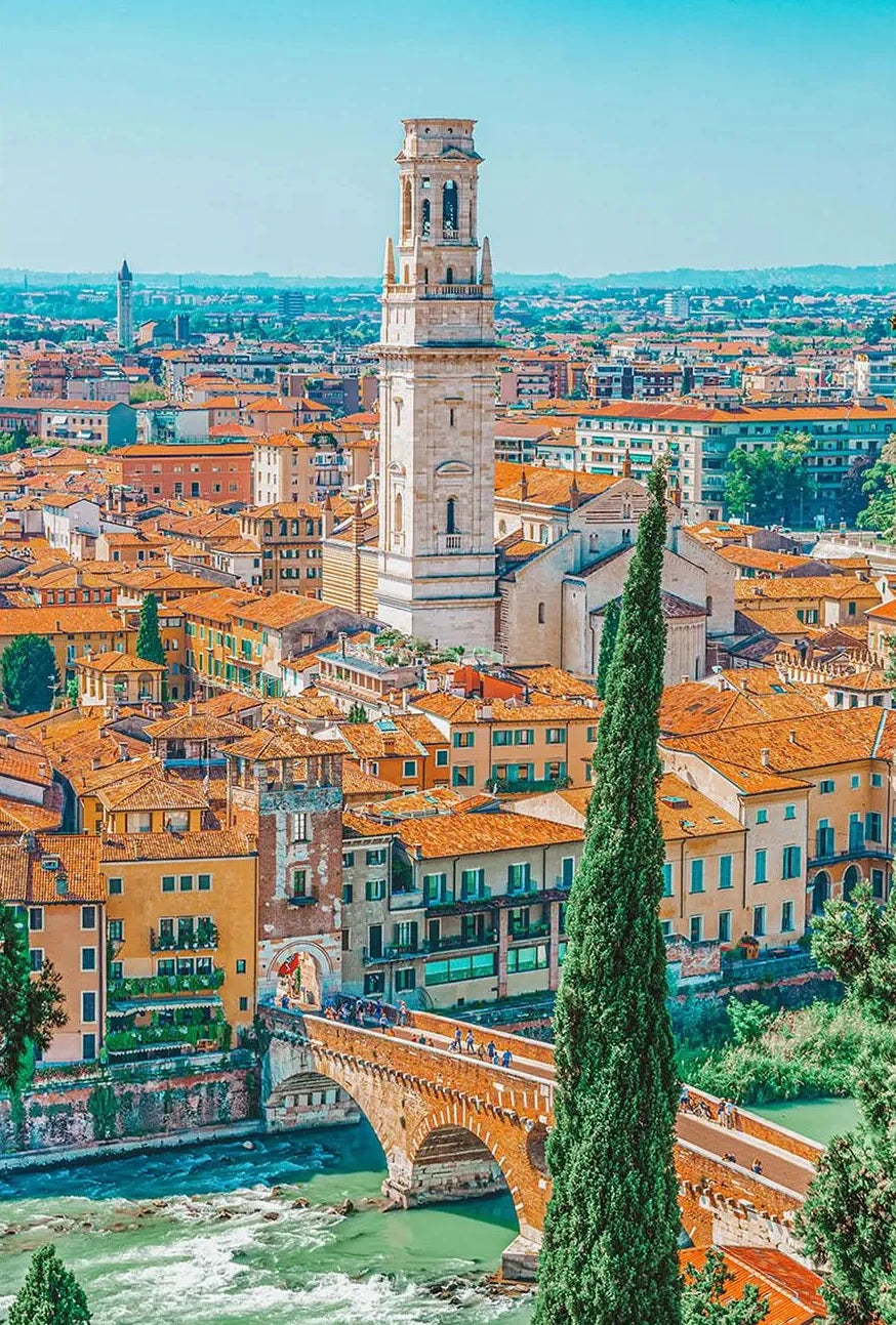 Cityscape with a tall tower and a river, featuring buildings with orange roofs.