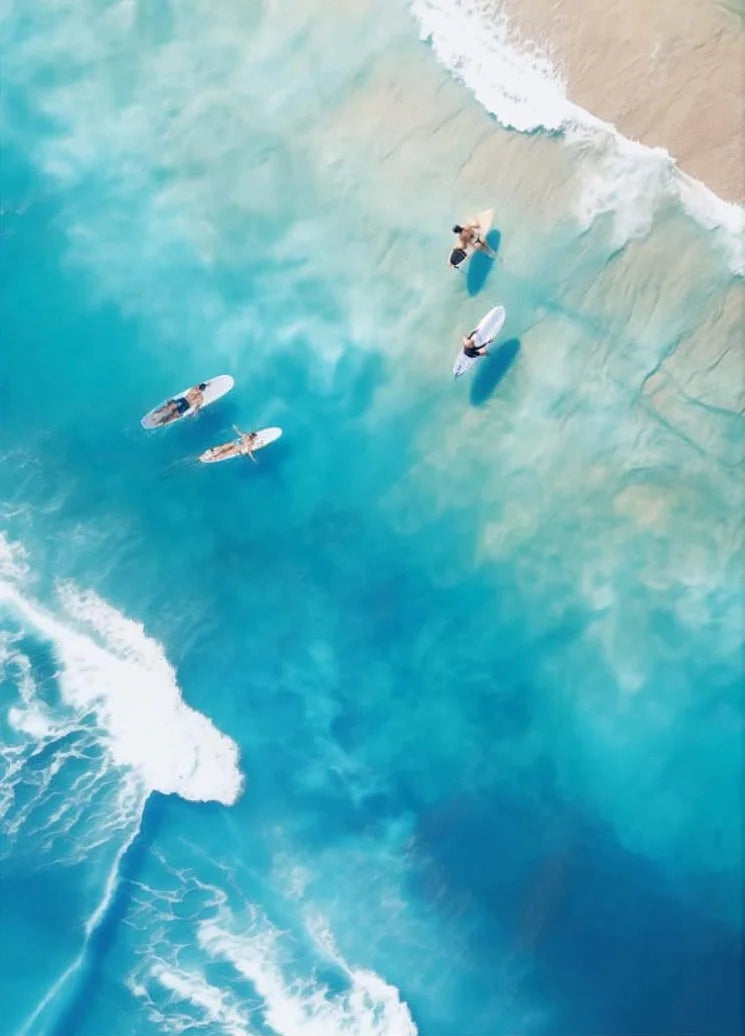 People paddleboarding on a clear blue ocean with a sandy beach in the background.
