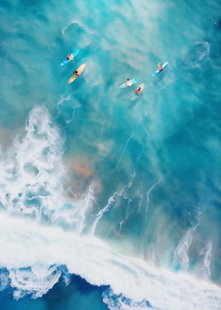 Aerial view of people kayaking in a turquoise ocean with white waves.