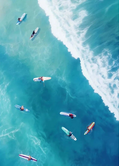 Aerial view of surfers on their boards in the ocean with clear blue water and white waves.