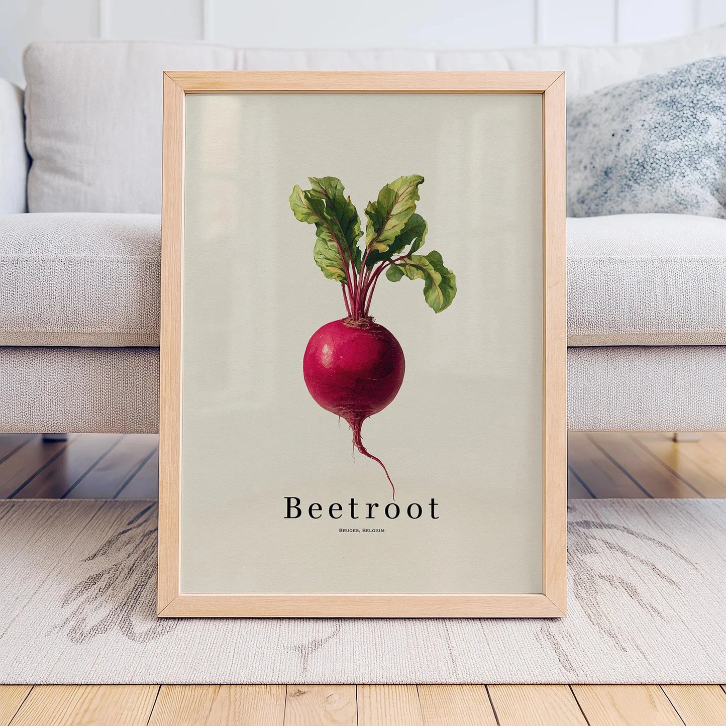 Framed artwork of a beetroot on a light background, placed on a wooden floor with a sofa in the background.