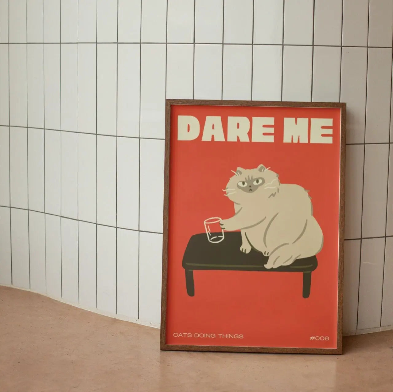 Framed poster with a cat illustration and 'Dare Me' text on a tiled wall.