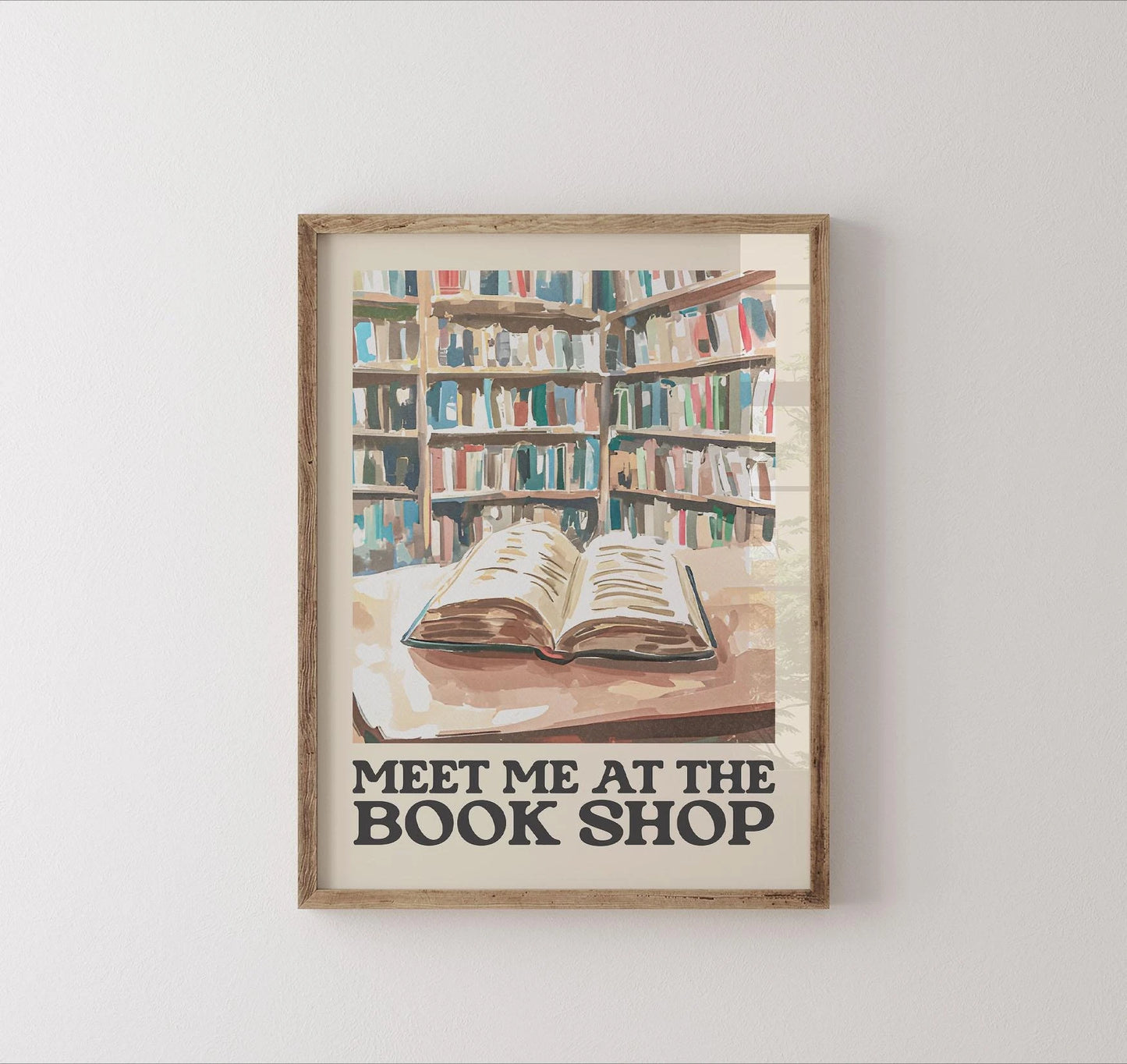 Framed artwork of a bookshelf with an open book and 'Meet Me at the Book Shop' text on a white wall.