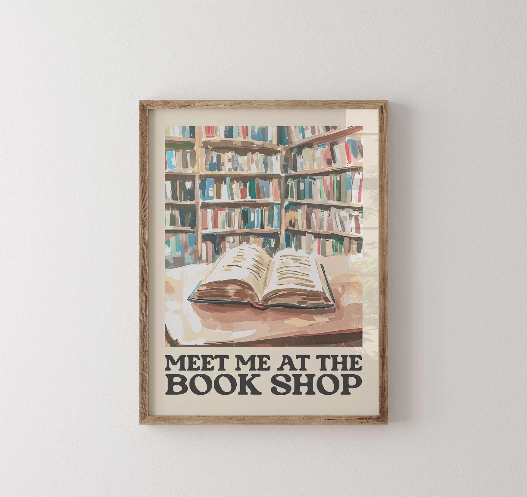 Framed artwork of a bookshelf with an open book and 'Meet Me at the Book Shop' text on a white wall.