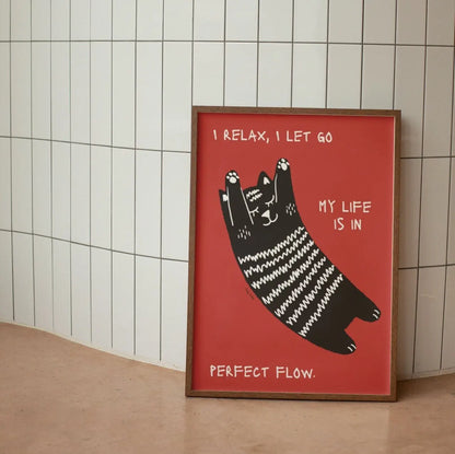 Framed artwork with a black cat illustration and text on a red background, leaning against a tiled wall.