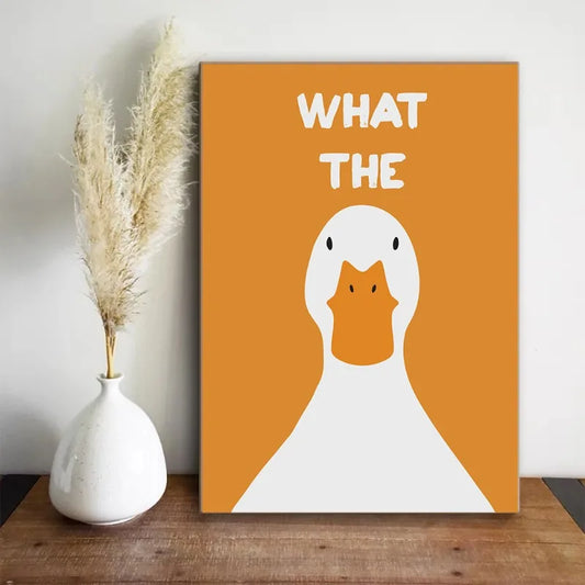 Canvas print with a duck illustration and 'WHAT THE' text on an orange background, placed on a wooden surface next to a white vase with dried plants. Canvas & Curio
