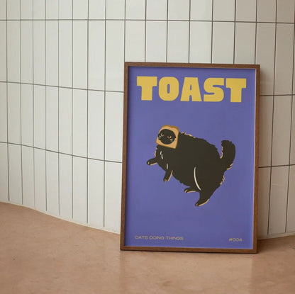 Framed artwork with a cat illustration and 'TOAST' text on a blue background, leaning against a tiled wall.