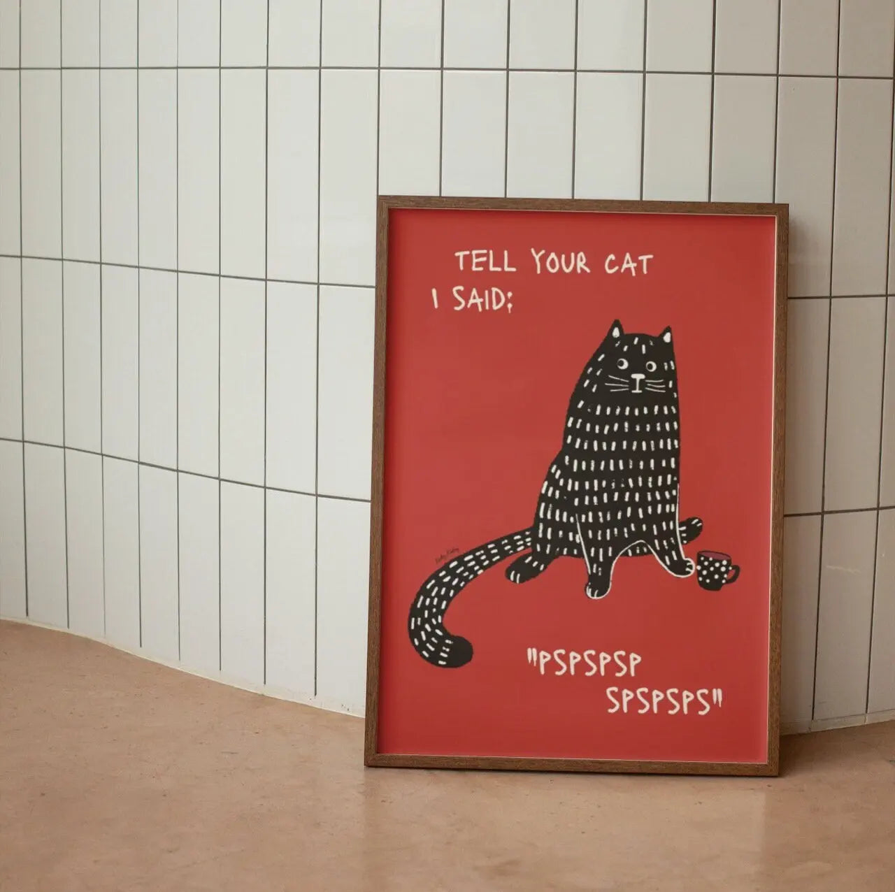 Framed poster with a black cat illustration and text on a red background, leaning against a tiled wall.