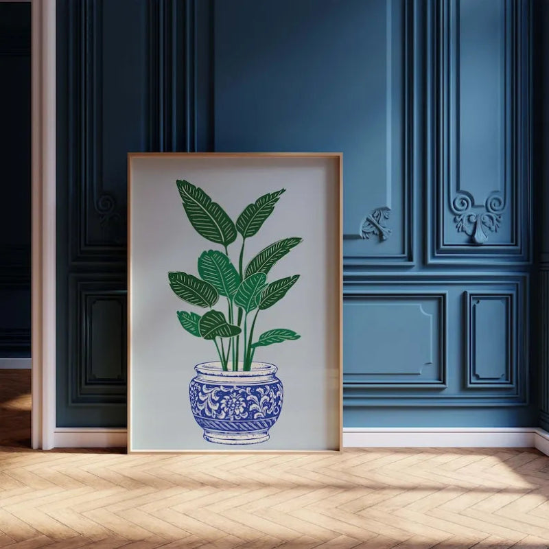 Framed artwork of a potted plant on a wooden floor with a blue wall in the background