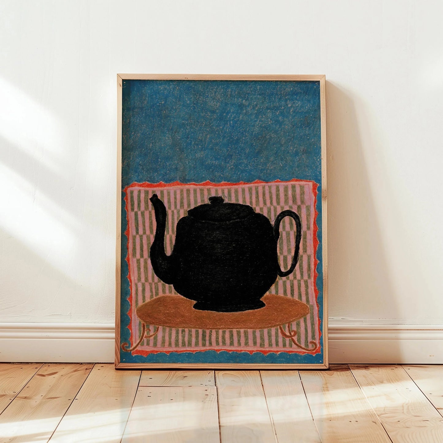 Framed artwork of a black teapot on a colorful background in a room with wooden floor and white walls.