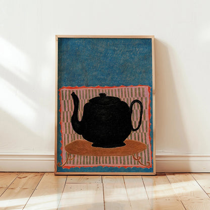 Framed artwork of a black teapot on a colorful background in a room with wooden floor and white walls.