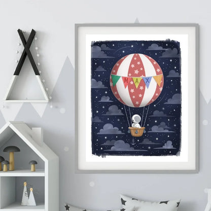 Framed artwork of a hot air balloon with colorful flags against a starry night sky, displayed on a wall.