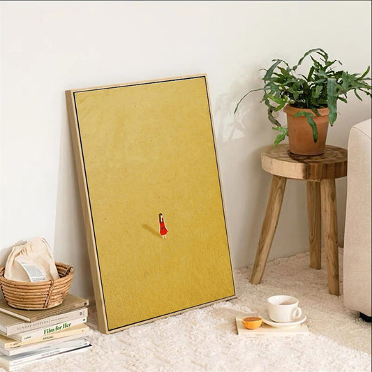Yellow framed artwork with a red figure on a white wall, next to a plant and small table. Canvas & Curio