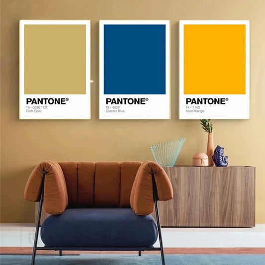 Three Pantone color posters on a wall with a modern chair and cabinet below. Canvas & Curio